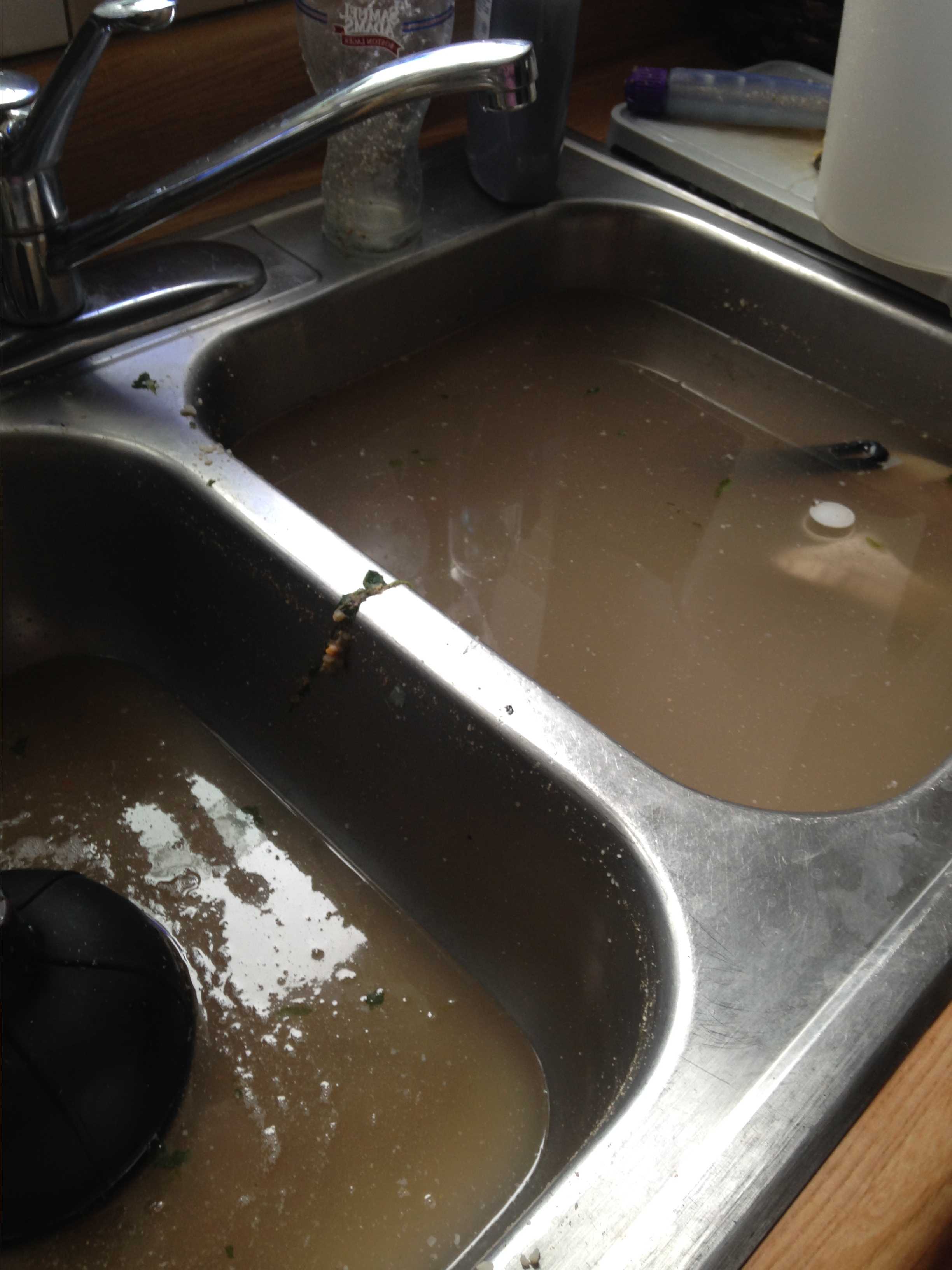 black kitchen sink clogged designed in double shape with two deep parts ffull with dirty water and a stainless faucet